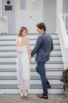 a bride and groom hold hands as they stand on the steps of a white house