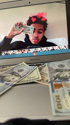 a laptop computer with money on top of it and a man's face in the screen