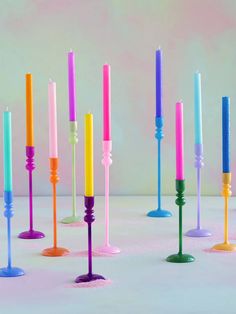 there are many different colored candles in the same row and one is pink, blue, yellow, green, orange