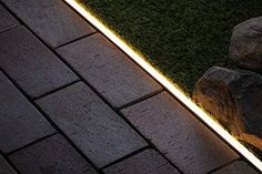 a light shines on the side of a brick walkway next to some rocks and grass