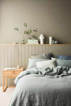 a bed with green sheets and pillows next to a wooden shelf filled with potted plants