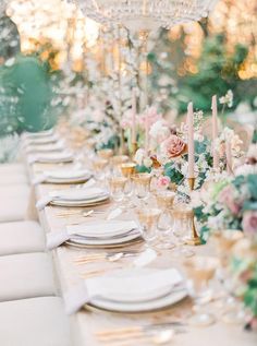 a long table is set with white and pink flowers, gold chargers and candles for an elegant wedding reception