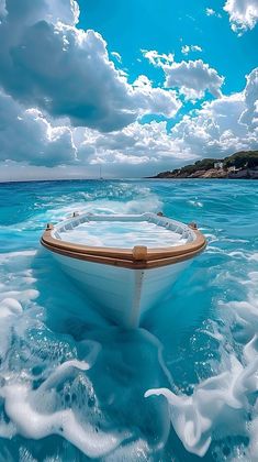 a boat floating on top of the ocean under a blue sky with clouds above it