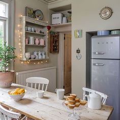 a kitchen table with plates and cups on it next to an open refrigerator freezer