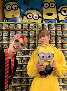 two people standing next to each other in front of stacks of mugs with minion faces on them