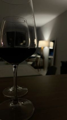 a glass of red wine sitting on top of a wooden table next to a lamp