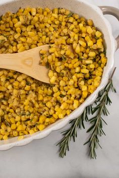 a large pot filled with corn and topped with a wooden spoon next to a sprig of rosemary