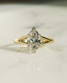 a yellow gold engagement ring with two pear shaped diamonds on the side, sitting on a marble surface