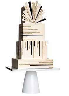 a stack of books sitting on top of a white cake stand with black and gold decorations