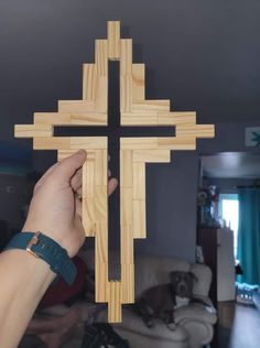 a person holding up a wooden cross in their hand with a dog laying on the couch behind it