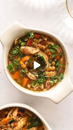 two bowls filled with chicken and vegetable soup on top of a white countertop next to a glass of water