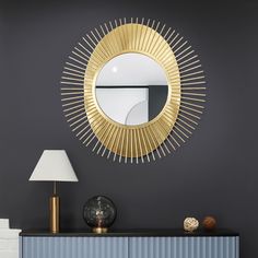 a gold sunburst mirror on the wall above a blue dresser with a lamp