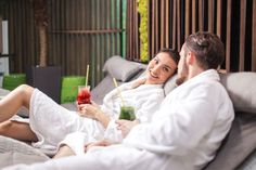 a man and woman laying in bed with drinks