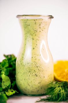 a glass jar filled with dressing next to lemons and parsley