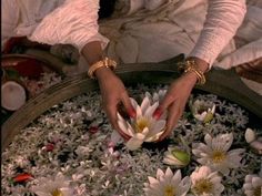 a woman is holding flowers in a large metal pot with water inside it and her hands are on the flower petals