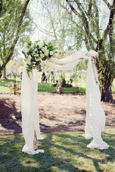 an outdoor wedding ceremony with white drapes and greenery on the trees, decorated with flowers