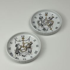 two white plates with black and gold designs on them, one is holding a clock