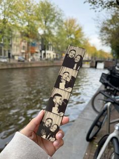 a person holding up a piece of paper with pictures of people on it in front of some water