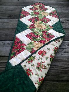 a quilted table runner with red and green flowers on it, sitting on a wooden floor