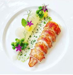 a white plate topped with meat covered in sauce and garnished with green peas