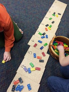 two children playing with blocks and numbers on the floor next to a basket full of dices