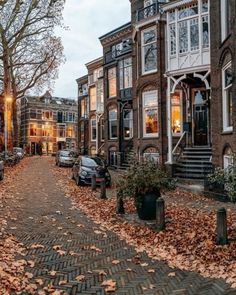 a cobblestone street lined with parked cars in front of tall brick buildings at dusk