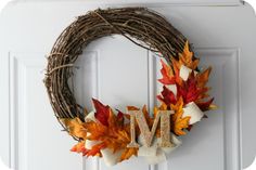 a wreath with the letter m on it and fall leaves hanging from it's front door