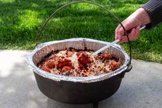 a person is cutting into some food in a large metal pot on the ground outside