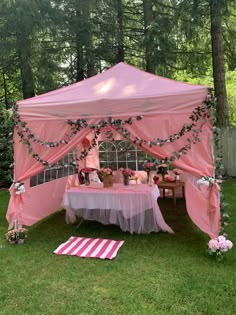 a pink tent is set up in the grass with flowers and greenery on it