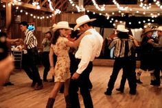 a man and woman dancing on a dance floor with lights strung over the top of them