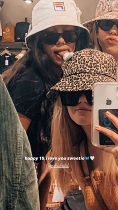 three women wearing hats and sunglasses taking a selfie with their cell phone in front of them