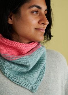 a woman wearing a knitted cowl with a pink and blue scarf around her neck