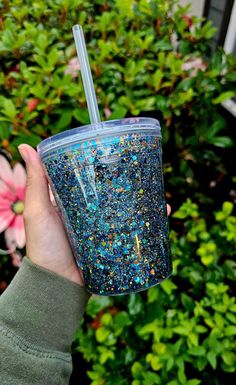 a person holding up a blue and gold glittered cup with a straw in it