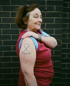 a woman with a cross tattoo on her arm standing in front of a brick wall