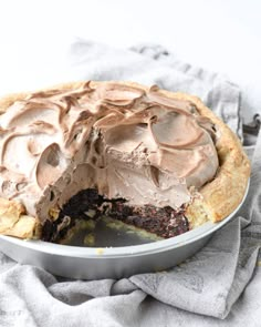 a pie with chocolate frosting in a pan on top of a table next to a gray towel