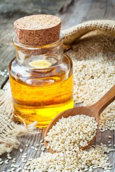 sesame seed oil in a glass bottle next to a wooden spoon and sack of seeds