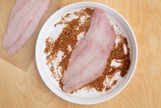 two pieces of meat sit in a white bowl on a wooden table next to some seasoning