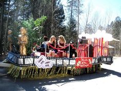 three women sitting on top of a float in the middle of a road with decorations