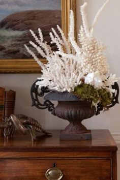 a vase filled with white flowers sitting on top of a wooden dresser next to a painting