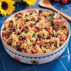 a bowl of pasta with meat and vegetables on the table next to sunflowers