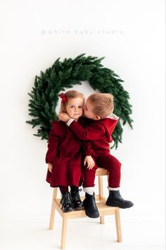 two children sitting on a chair in front of a christmas wreath