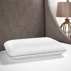 a close up of a pillow on a bed next to a night stand with a lamp