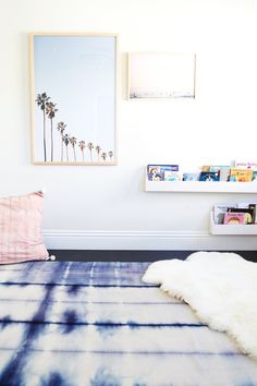 a bed room with a neatly made bed next to a wall mounted book shelf filled with books