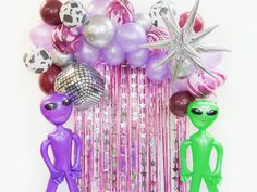 two alien figurines standing next to each other in front of balloons and streamers