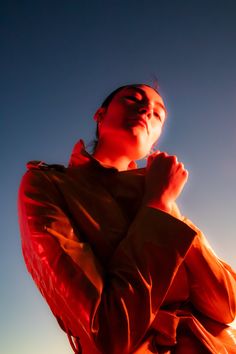 a woman standing in front of the sun with her hands folded up to her chest