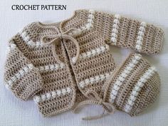 three crocheted sweaters sitting on top of a white cloth covered tablecloth