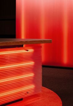 a red wall behind a counter with a wooden table in front of it and an orange light shining on the floor