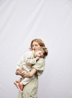 a woman holding a baby in her arms while standing against a white background with the back turned to the camera