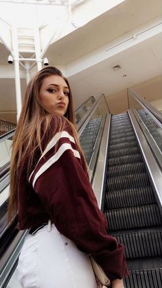 a woman standing on an escalator with her hands in her pockets