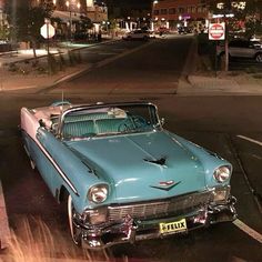 an old blue car is parked on the side of the road at night with its hood up